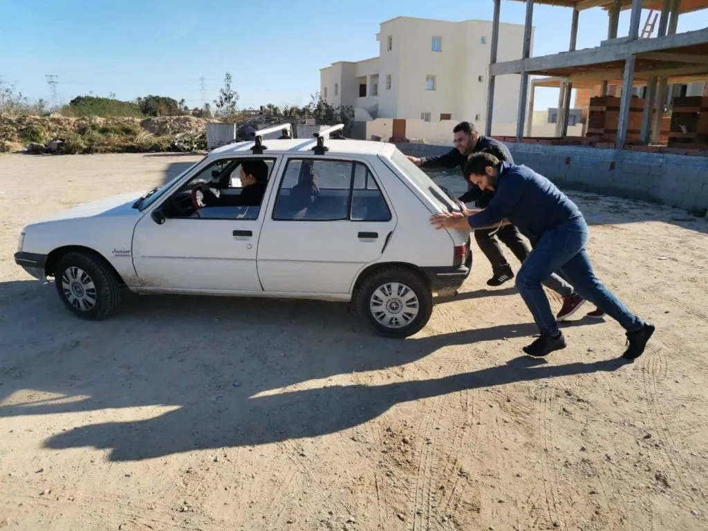 Deux développeurs du BearStudio poussant une Peugeot 205 en panne dans le désert tunisien lors d'une visite d'équipe